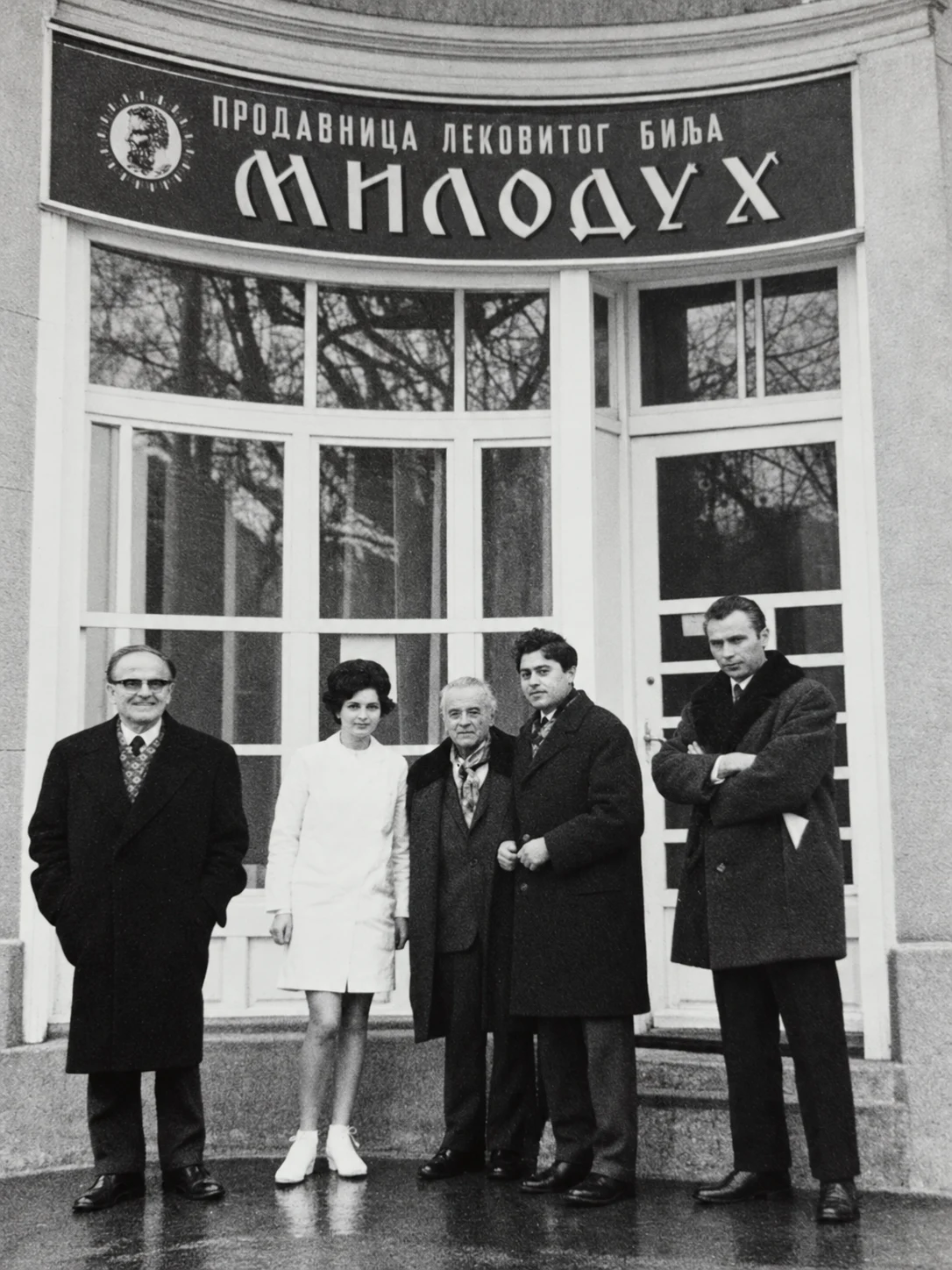 Arhivska crno-bela fotografija petoro ljudi ispred prodavnice lekovitog bilja Miloduh